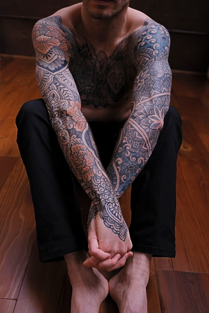 A man with two full ornamental tattoo sleeves with geometric patterns and flowers